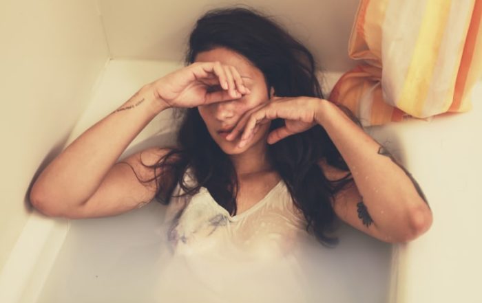 clothed woman in bath looking overwhelmed